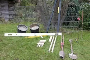 So errichten Sie fachmännisch einen soliden Doppelstabmattenzaun "Vorbereitete Werkzeuge und Materialien für die Montage eines Doppelstabmattenzauns, inklusive Schaufeln, Wasserwaage und Pfosten.