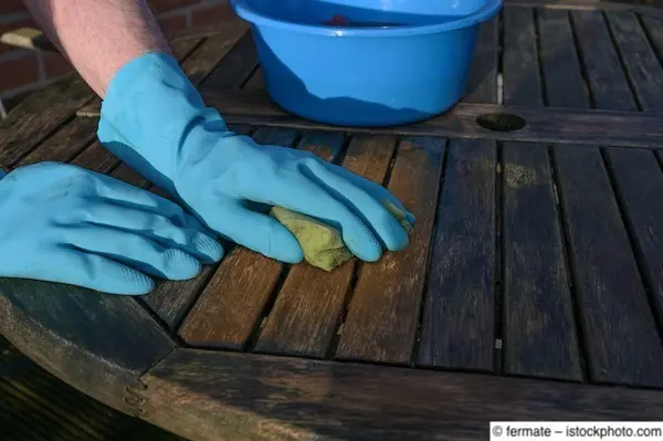 Verwitterter Holzgartentisch wird gründlich von Hand gesäubert
