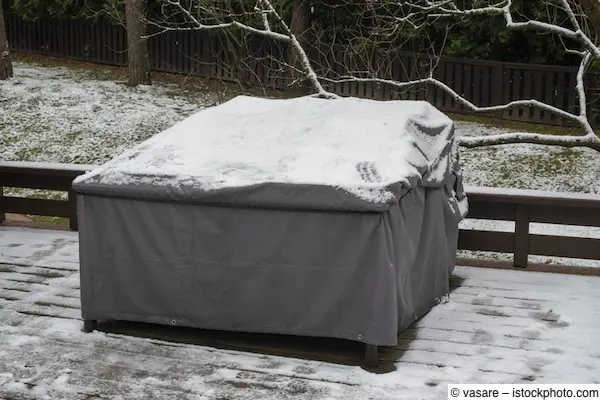Mit Schutzhülle abgedeckte Gartenmöbel auf schneebedeckter Terrasse