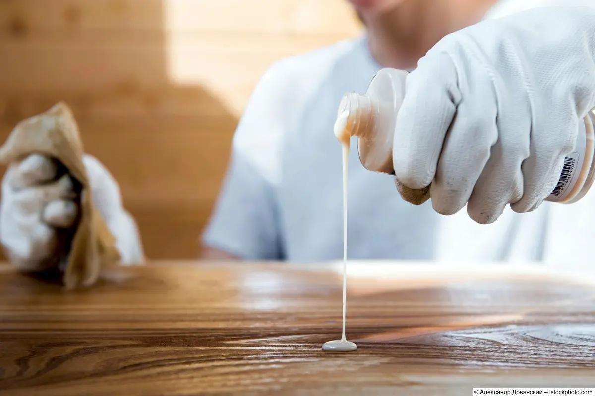 Mädchen in Arbeitshandschuhen gießt Öl auf eine Holztischplatte