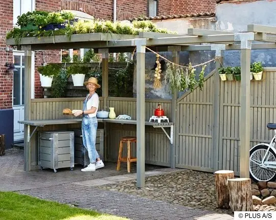 Innenhof mit Gartenküche, eingerahmt von pergolaartigem Balkengerüst mit Sichtblenden