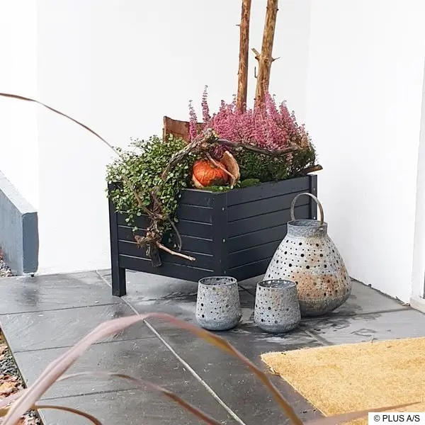 Winterlicher Blumenkasten im Hauseingangsbereich Winterlicher Eingangsbereich mit Blumenkasten, Heidekraut, Kürbis und drei metallenen Windlichtern auf grauen Fliesen.