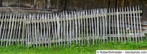 Alter, stark verwitterter grauer Holzzaun vor Scheune