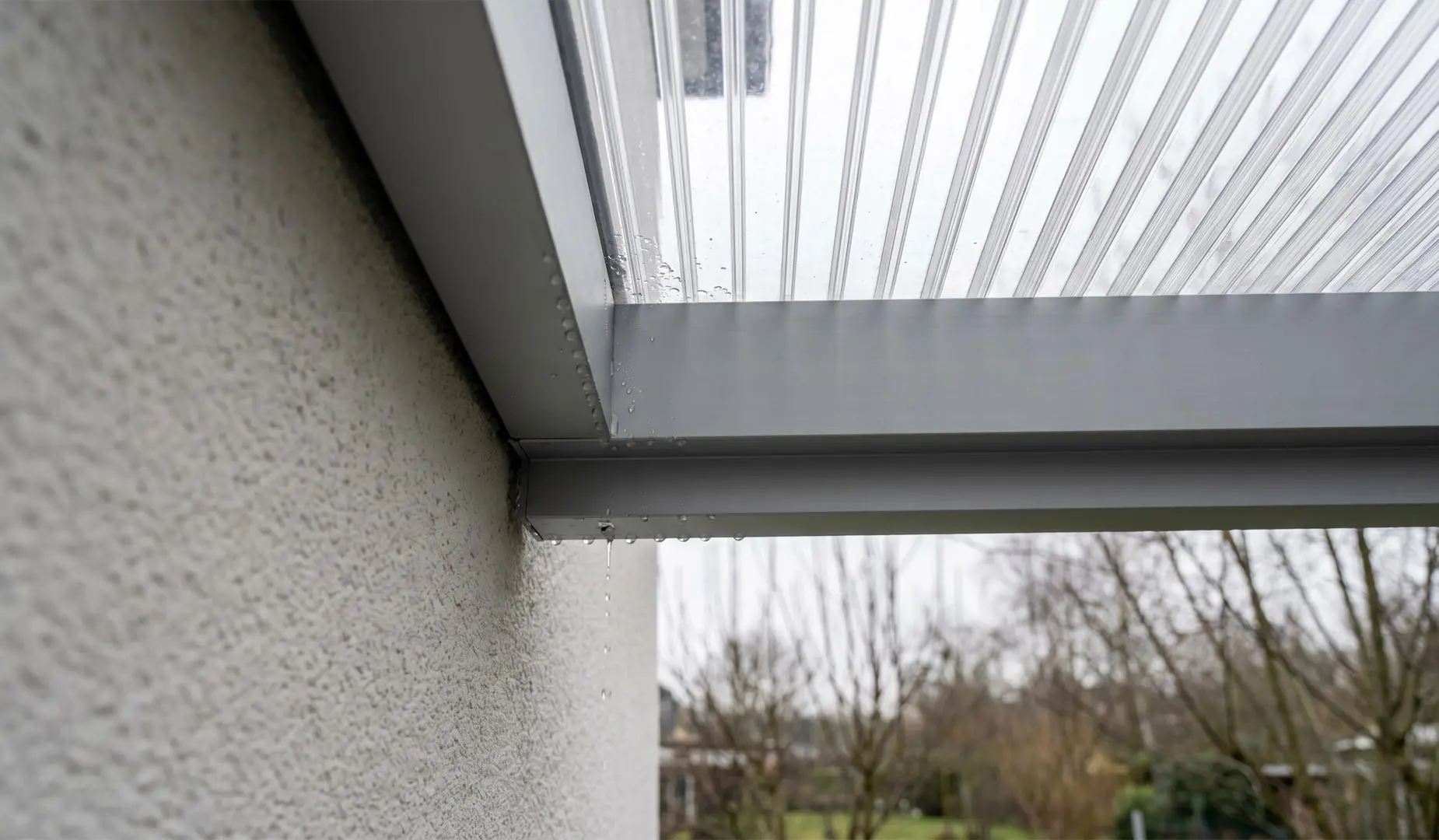Wandanschluss eines Doppelstegplatten-Terrassendachs nach starkem Regen mit sichtbaren Wassertropfen am Profilrand