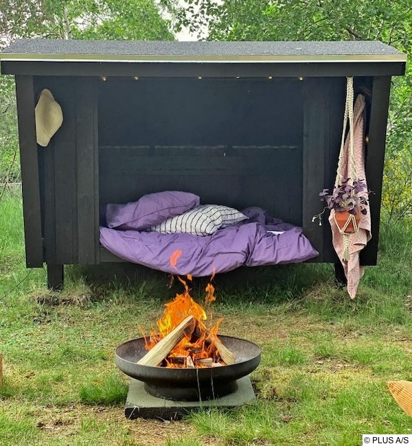 "Gemütliche Gartenhütte mit überdachtem Schlafplatz und Lagerfeuer, ideal für Outdoor-Übernachtungen in der Natur.